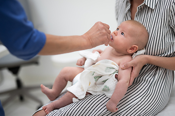 Image showing Pediatrician administring oral vaccination against rotavirus infection to little baby in presence of his mother. Children health care and disease prevention