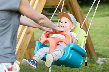 Image showing Mother pushing her infant baby boy child on a swing on playground outdoors.