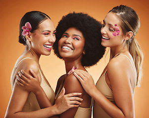 Image showing Beauty, flowers and women in makeup, diversity and models on orange studio background. Smile, skincare and happy, young and elegant female friends posing together with orchids after spa treatment.