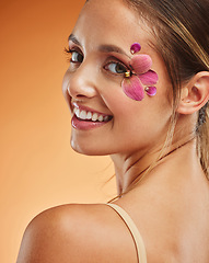 Image showing Beauty, makeup and creative with woman petals on face for design, flowers and natural cosmetics against orange background in studio. Spring, skincare and smile with girl for color, model and orchid