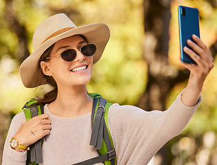Image showing Nature, phone selfie and woman hiking with hat, sunglasses and smile, adventure in forest or woods in summer. Freedom, peace and exercise, a walk in the trees to relax mindset and enjoy weekend time.