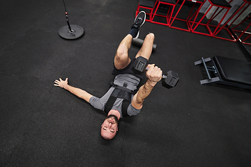 Image showing A muscular man is focused on working out with dumbbells in a modern gym, showing his determination and commitment to his fitness regimen.