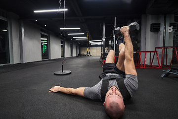 Image showing A muscular man is focused on working out with dumbbells in a modern gym, showing his determination and commitment to his fitness regimen.