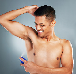 Image showing Happy, smile and man with deodorant spray for hygiene, fresh scent and fragrance after a shower. Happiness, clean and guy spraying his armpit to prevent odor or smell isolated by a gray background.
