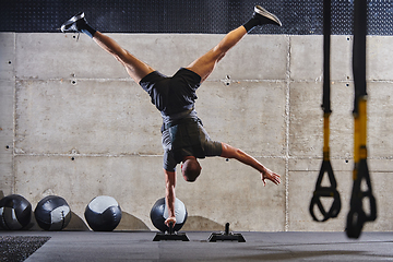 Image showing A muscular man in a handstand position, showcasing his exceptional balance and body control while performing a variety of exercises to enhance his overall body stability and strength in a modern gym