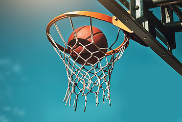 Image showing Basketball, goal and target in basket for sports match training on outdoor athletic court. Aim, score and winner with ball dunk in net at competition practice from low angle with blue sky.