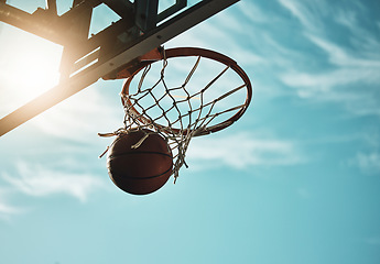 Image showing Below, basketball and net with sky in summer for shooting, scoring and points to win game. Hoop, rim and ball in closeup at basketball court for sports, competition or workout at playground, outdoor