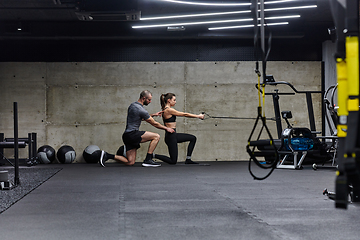 Image showing A muscular man assisting a fit woman in a modern gym as they engage in various body exercises and muscle stretches, showcasing their dedication to fitness and benefiting from teamwork and support