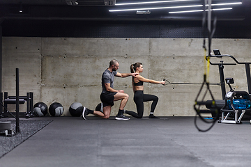 Image showing A muscular man assisting a fit woman in a modern gym as they engage in various body exercises and muscle stretches, showcasing their dedication to fitness and benefiting from teamwork and support