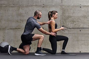 Image showing A muscular man assisting a fit woman in a modern gym as they engage in various body exercises and muscle stretches, showcasing their dedication to fitness and benefiting from teamwork and support