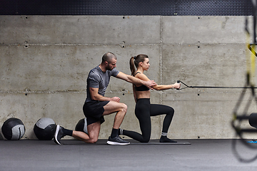 Image showing A muscular man assisting a fit woman in a modern gym as they engage in various body exercises and muscle stretches, showcasing their dedication to fitness and benefiting from teamwork and support