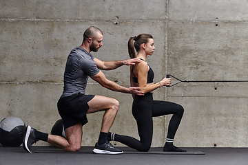 Image showing A muscular man assisting a fit woman in a modern gym as they engage in various body exercises and muscle stretches, showcasing their dedication to fitness and benefiting from teamwork and support