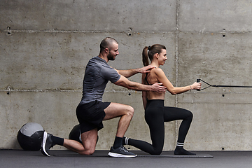 Image showing A muscular man assisting a fit woman in a modern gym as they engage in various body exercises and muscle stretches, showcasing their dedication to fitness and benefiting from teamwork and support