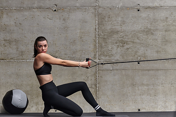 Image showing A fit woman in a modern gym performs arm exercises with determination, showcasing her strength and sculpted muscles as she works towards her fitness goals.