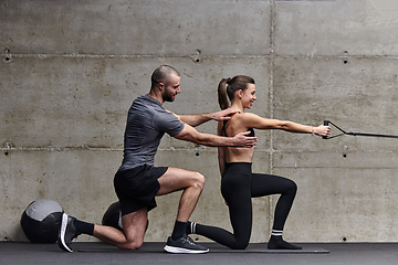 Image showing A muscular man assisting a fit woman in a modern gym as they engage in various body exercises and muscle stretches, showcasing their dedication to fitness and benefiting from teamwork and support