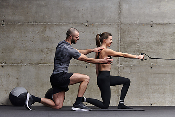 Image showing A muscular man assisting a fit woman in a modern gym as they engage in various body exercises and muscle stretches, showcasing their dedication to fitness and benefiting from teamwork and support