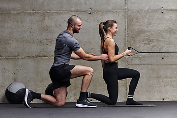 Image showing A muscular man assisting a fit woman in a modern gym as they engage in various body exercises and muscle stretches, showcasing their dedication to fitness and benefiting from teamwork and support