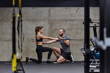 Image showing A muscular man assisting a fit woman in a modern gym as they engage in various body exercises and muscle stretches, showcasing their dedication to fitness and benefiting from teamwork and support