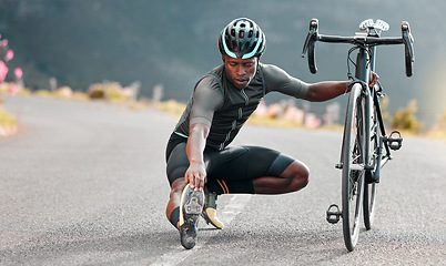 Image showing Outdoor, cycling and cyclist doing stretching exercise by his bicycle on road in mountain. Sports, training for fitness and man athlete doing warm up before cardio cycle workout with bike in nature.