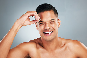 Image showing Portrait of a man tweezing his eyebrow with a tweezer in studio with gray background. Happy, smile and young guy plucking brow for hair removal for grooming, cleaning and hygiene routine or self care