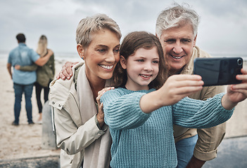 Image showing Phone, selfie and grandparents with a child at the beach while on family adventure, journey or holiday. Happy, smile and senior couple in retirement taking picture with girl while on seaside vacation