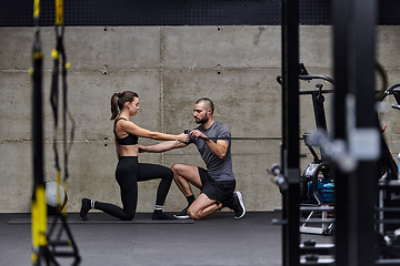 Image showing A muscular man assisting a fit woman in a modern gym as they engage in various body exercises and muscle stretches, showcasing their dedication to fitness and benefiting from teamwork and support