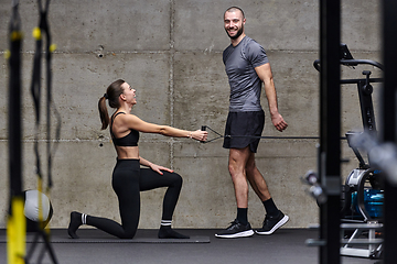 Image showing A muscular man assisting a fit woman in a modern gym as they engage in various body exercises and muscle stretches, showcasing their dedication to fitness and benefiting from teamwork and support