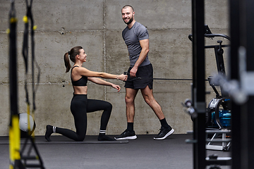 Image showing A muscular man assisting a fit woman in a modern gym as they engage in various body exercises and muscle stretches, showcasing their dedication to fitness and benefiting from teamwork and support