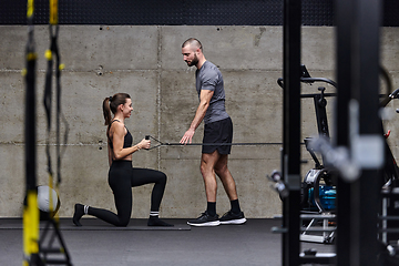 Image showing A muscular man assisting a fit woman in a modern gym as they engage in various body exercises and muscle stretches, showcasing their dedication to fitness and benefiting from teamwork and support