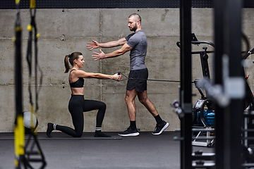 Image showing A muscular man assisting a fit woman in a modern gym as they engage in various body exercises and muscle stretches, showcasing their dedication to fitness and benefiting from teamwork and support