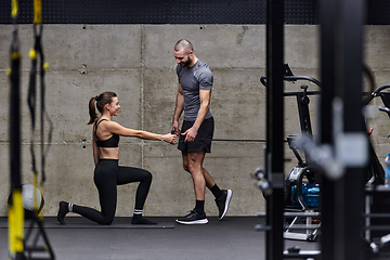 Image showing A muscular man assisting a fit woman in a modern gym as they engage in various body exercises and muscle stretches, showcasing their dedication to fitness and benefiting from teamwork and support