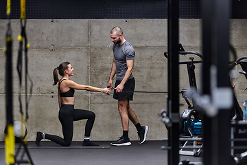 Image showing A muscular man assisting a fit woman in a modern gym as they engage in various body exercises and muscle stretches, showcasing their dedication to fitness and benefiting from teamwork and support