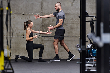 Image showing A muscular man assisting a fit woman in a modern gym as they engage in various body exercises and muscle stretches, showcasing their dedication to fitness and benefiting from teamwork and support