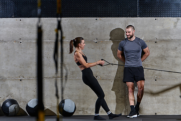 Image showing A muscular man assisting a fit woman in a modern gym as they engage in various body exercises and muscle stretches, showcasing their dedication to fitness and benefiting from teamwork and support