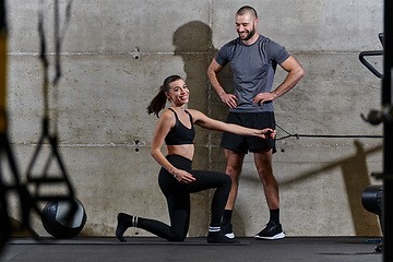 Image showing A muscular man assisting a fit woman in a modern gym as they engage in various body exercises and muscle stretches, showcasing their dedication to fitness and benefiting from teamwork and support