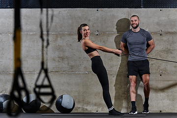 Image showing A muscular man assisting a fit woman in a modern gym as they engage in various body exercises and muscle stretches, showcasing their dedication to fitness and benefiting from teamwork and support