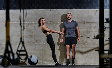 Image showing A muscular man assisting a fit woman in a modern gym as they engage in various body exercises and muscle stretches, showcasing their dedication to fitness and benefiting from teamwork and support