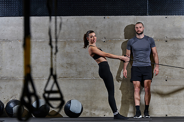 Image showing A muscular man assisting a fit woman in a modern gym as they engage in various body exercises and muscle stretches, showcasing their dedication to fitness and benefiting from teamwork and support