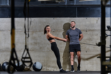 Image showing A muscular man assisting a fit woman in a modern gym as they engage in various body exercises and muscle stretches, showcasing their dedication to fitness and benefiting from teamwork and support