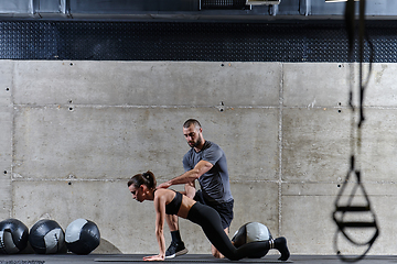 Image showing A muscular man assisting a fit woman in a modern gym as they engage in various body exercises and muscle stretches, showcasing their dedication to fitness and benefiting from teamwork and support