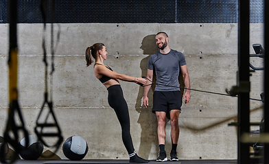 Image showing A muscular man assisting a fit woman in a modern gym as they engage in various body exercises and muscle stretches, showcasing their dedication to fitness and benefiting from teamwork and support