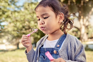 Image showing Nature, fun and a girl blowing bubbles in an outdoor park on a happy summer weekend. Sun, fun and a blow a soap bubble, freedom playing in the garden, a cute child in field with trees and sunshine.