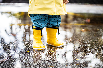 Image showing Small infant boy wearing yellow rubber boots and yellow waterproof raincoat standing in puddle on a overcast rainy day. Child in the rain.