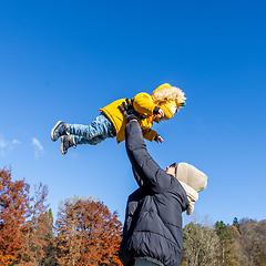 Image showing More, more,...mum, that's fun. Happy young mother throws her cute little baby boy up in the air. Mother's Day, Mather and her son baby boy playing and hugging outdoors in nature in fall.