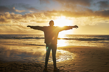 Image showing Worship, sunrise and silhouette of man at the beach standing with arms raised. Faith, religious and spiritual person looking at sun, ocean and sky in morning feeling calm, peace and hope in nature