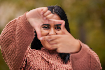 Image showing Hands frame, woman and eyes look through fingers while framing happy facial expression. Portrait of young indian girl, pose behind hand gesture and smile against blur bokeh nature background outside