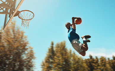 Image showing Basketball, sports and dunk with a man athlete jumping or flying through the air to score while playing on an outdoor court against the sky. Sport, fitness and exercise with a male basketball player