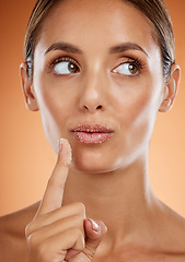 Image showing Face, beauty and idea with a model woman applying sugar lip balm her lips in studio on an orange background. Thinking, skin and mouth with an attractive young female posing for cosmetics or wellness