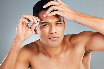 Image showing Beauty, grooming and eyebrow tweezers with a man in studio on a gray to remove hair from his eyebrows. Cosmetics, eyes and natural with a handsome young male taking care of his face alone inside