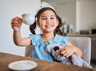 Image showing Tea party, happy girl and happiness of a young child on a home kitchen table with a smile. Play, fun and Asian kid from China with a tiara at a house smiling and playing with a cup and teddy bear